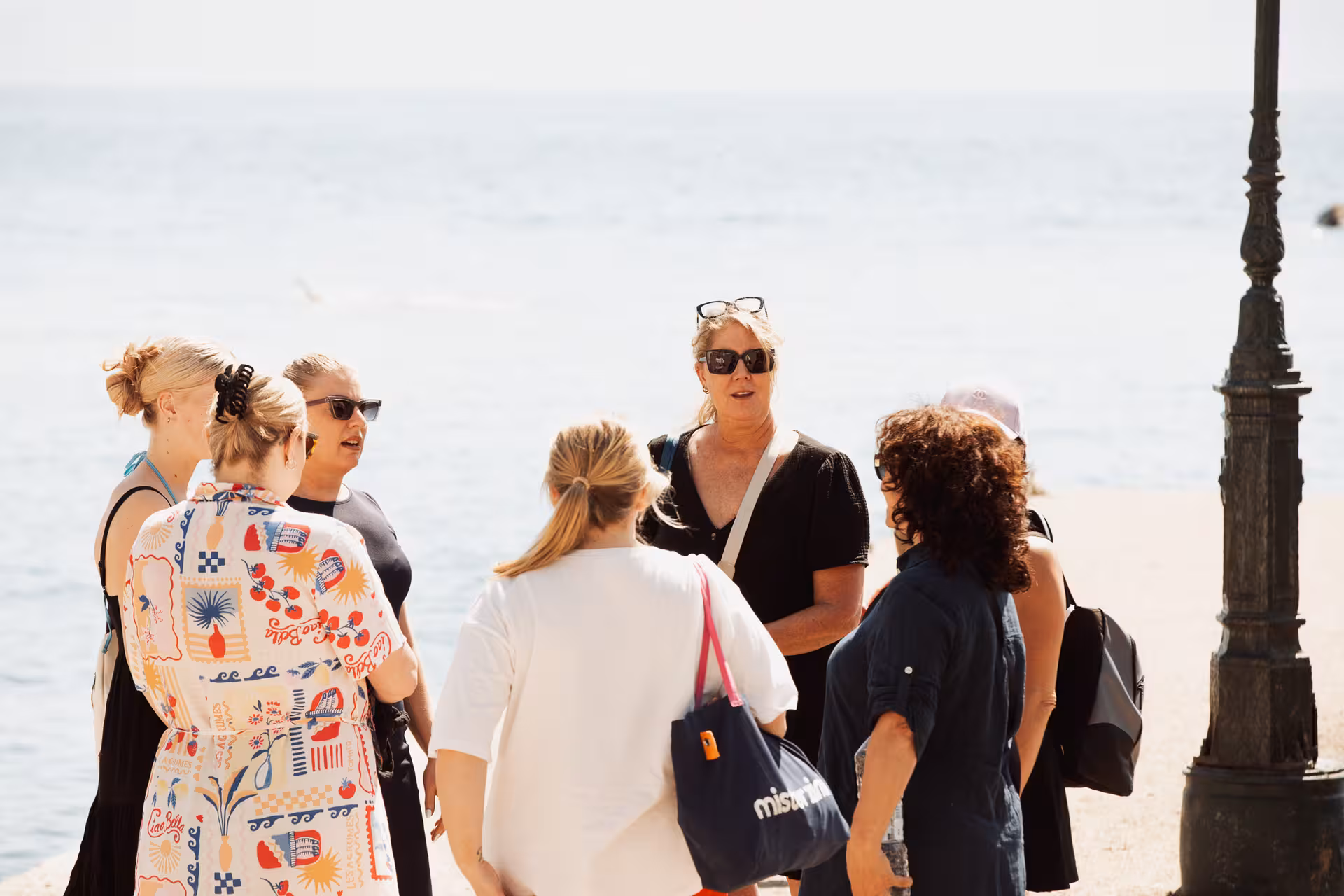 Small group of travelers gathered with guide on Ikaria beach promenade before exploring villages, Therma hot springs and taverna lunch