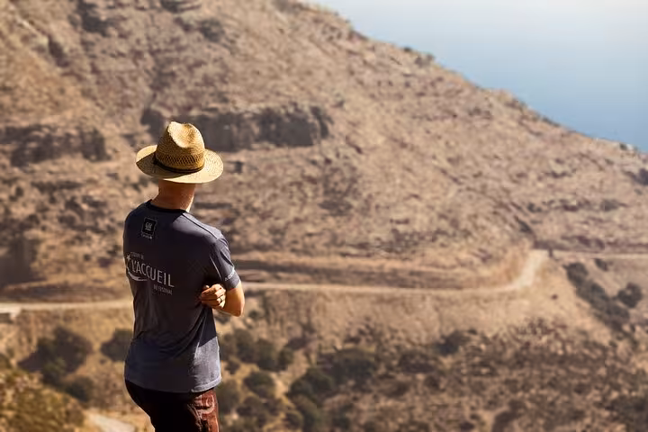 Traveler in sunhat admiring dramatic Ikaria coastline and winding cliff road on Randi’s Forest hike to Seychelles Beach by boat