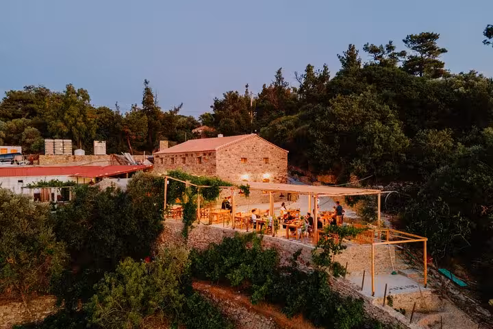 Outdoor terrace of a rustic family-run winery in Ikaria at sunset, with guests dining among hillside vineyards