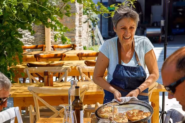 Local host in Ikaria serving freshly baked bread at a sunny outdoor taverna on the Ikaria Longevity forest and winery tour