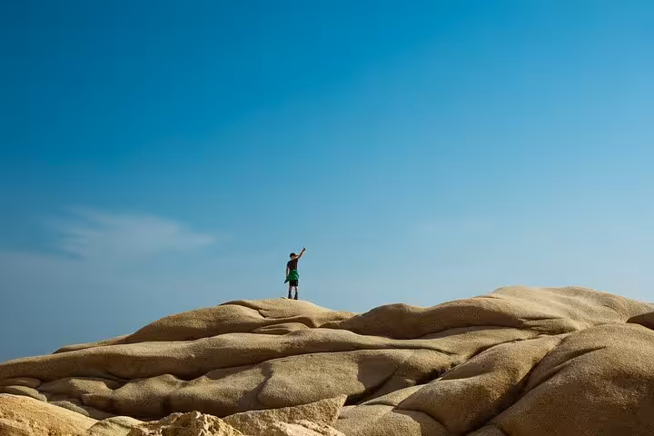 Hiker stands atop sculpted sandstone rocks on Ikaria’s west coast, enjoying panoramic Aegean Sea views on guided highlights tour