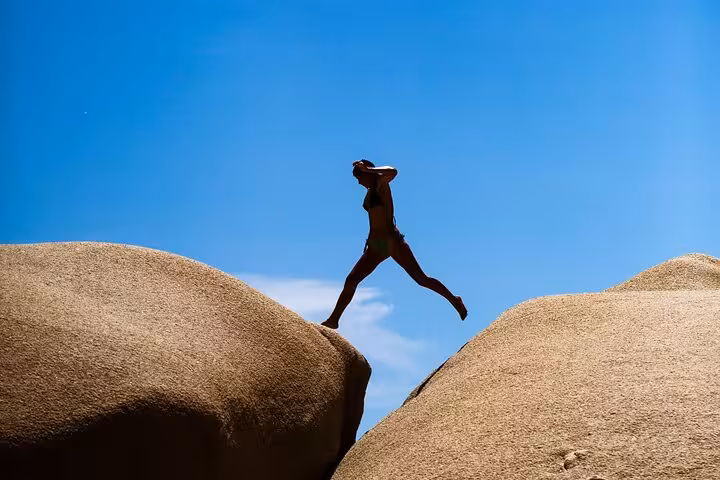 Traveler leaping between giant rock formations under blue skies on Ikaria’s wild west coast beach adventure tour