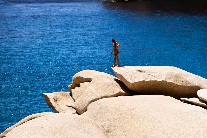 Traveler standing on sculpted granite cliffs above turquoise Aegean waters on Ikaria’s west side, perfect for swimming and photos