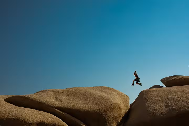 Traveler jumps between smooth rock formations under clear blue sky on Ikaria west side adventure tour with beaches and lunch