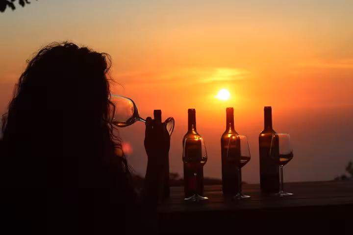 Traveler tasting local Ikaria wine at sunset, with bottles silhouetted against the Aegean Sea horizon