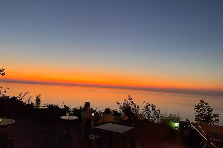 Guests relax on an Ikaria winery terrace at golden sunset, overlooking calm Aegean Sea on small-group wine tour