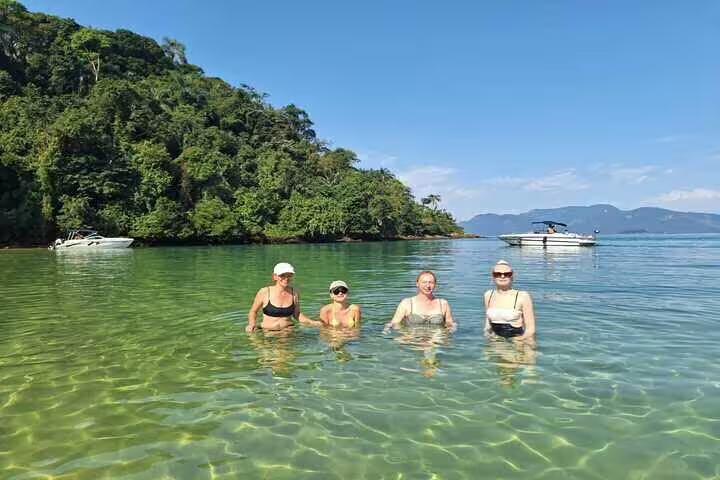 Visitors swimming in clear waters of Ilha Grande with lush green backdrop, part of Angra boat tour experience.