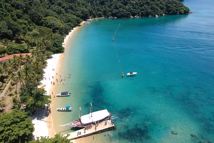 Beachgoers enjoy a sunny day on a pristine beach with turquoise waters, a key attraction for the Ilha Grande schooner ride.