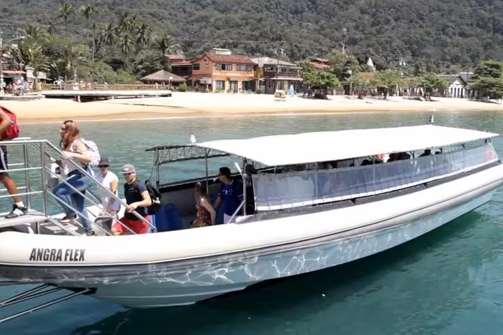 Tourists boarding a shuttle boat from Ilha Grande to Rio de Janeiro with scenic beach views in the background.