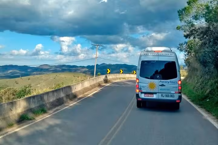 Scenic view of a shuttle bus traveling from Ilha Grande to Rio de Janeiro along a winding road with lush hillsides.
