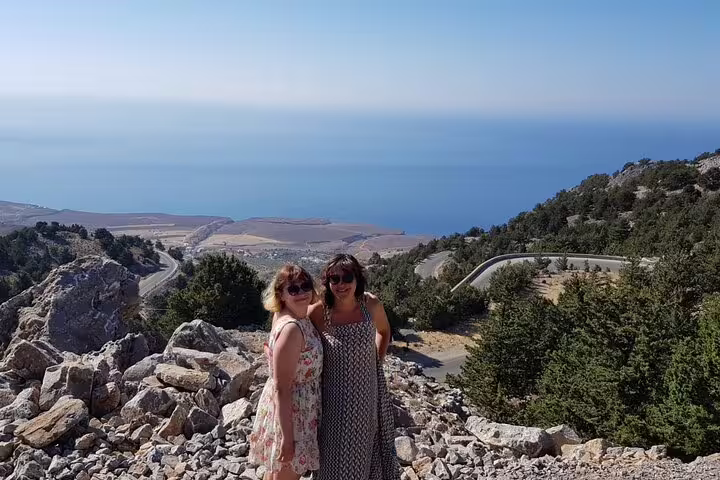 Two people smiling on a rocky viewpoint overlooking the expansive Imbros Gorge with the sea in the background.