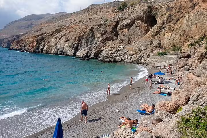 Relaxing beach scene near Imbros Gorge with sunbathers and turquoise waters, perfect for post-hike relaxation.