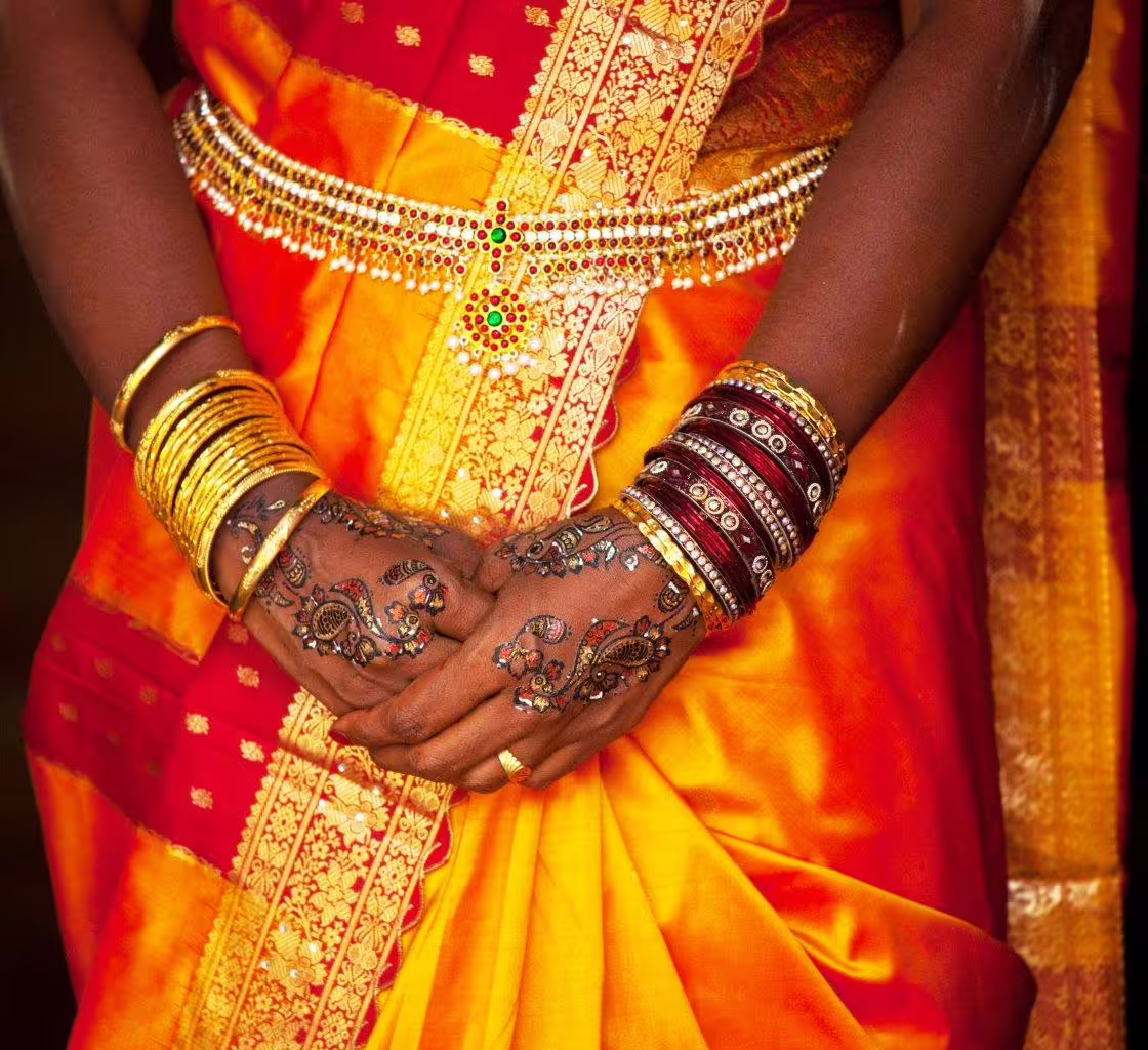 Close-up of a woman in a vibrant orange and red saree adorned with traditional jewelry and henna, symbolizing Indian culture.