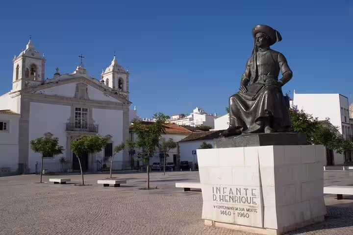 Statue of Infante D. Henrique in Lagos, Portugal, with historic church backdrop on Algarve tour from Lisbon.