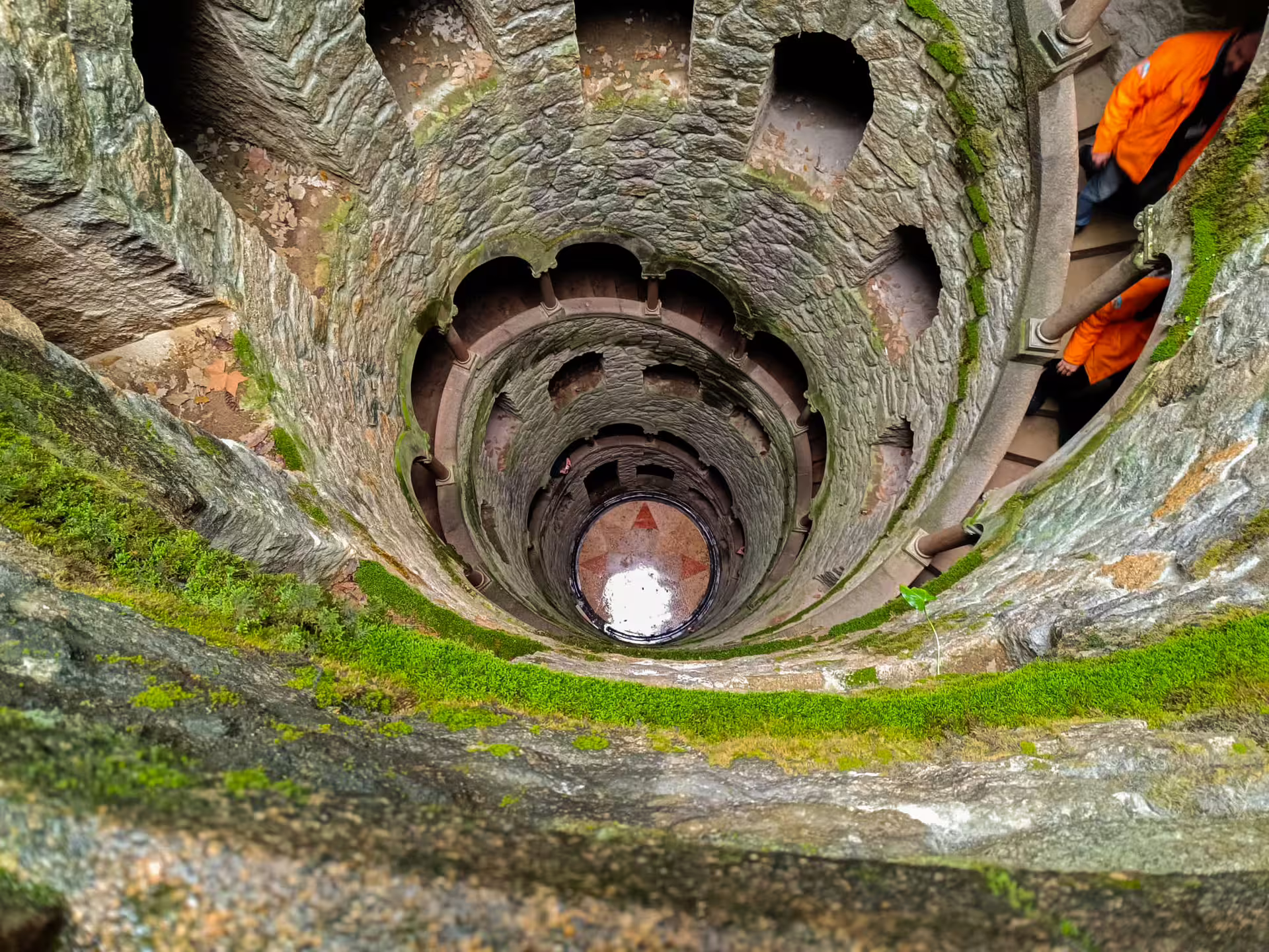 View of the mystical Initiation Well at Quinta da Regaleira, Sintra, highlighting its spiral staircase and mossy stone walls.