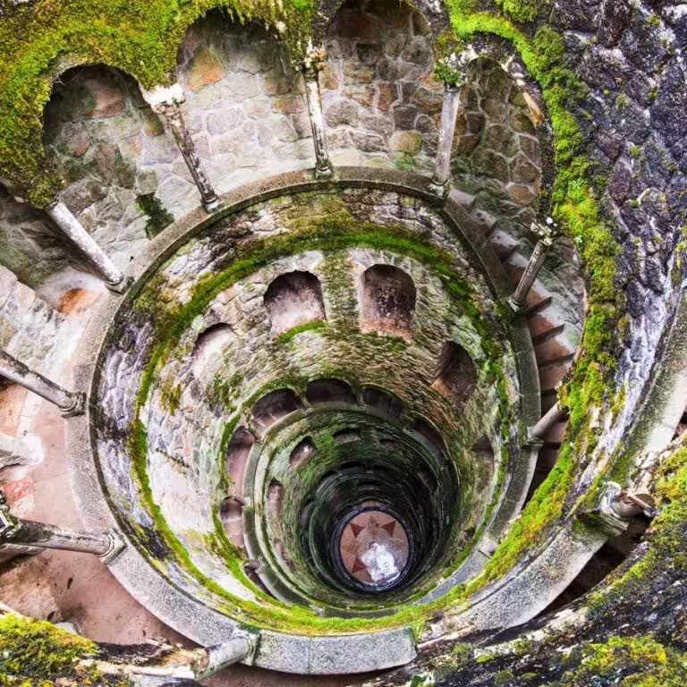 Explore the mystical Initiation Well at Quinta da Regaleira, Sintra, surrounded by lush greenery and stone arches.