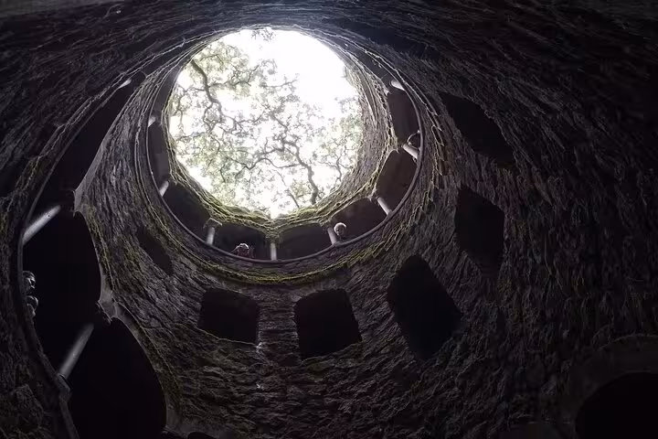 Looking up from the bottom of the Initiation Well in Quinta da Regaleira, highlighting the well's circular structure and natural light.