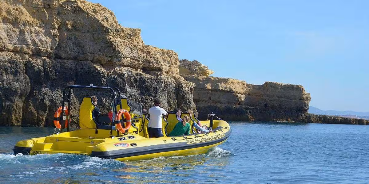 A yellow tour boat sails close to rocky cliffs on the scenic Insonia caves and dolphin watching experience.