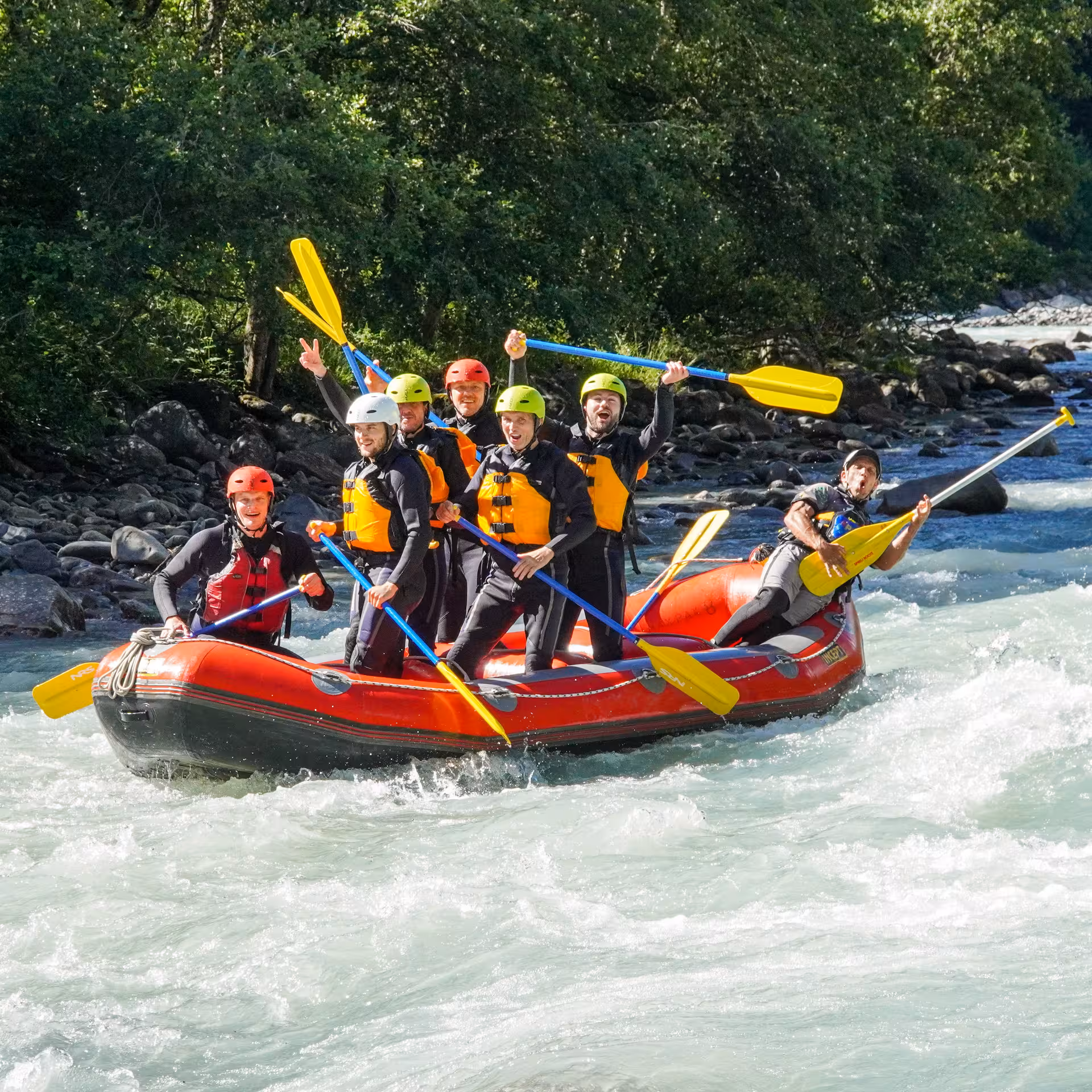 Excited group of rafters enjoying a sunny whitewater rafting adventure in Interlaken, showcasing teamwork and fun.