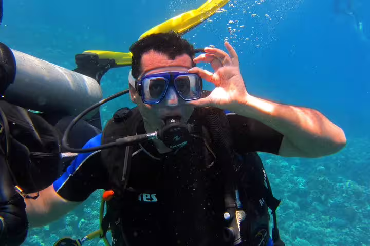First-time scuba diver giving OK hand signal in clear blue water on an intro diving and snorkeling tour