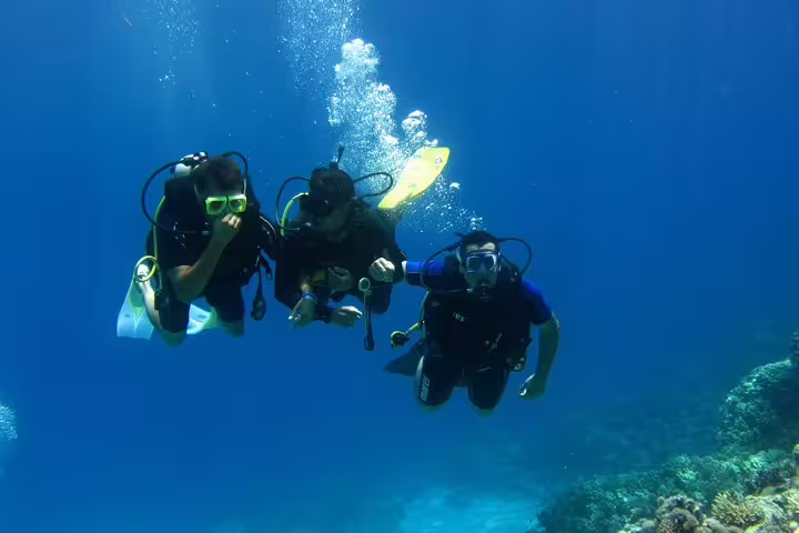 Three divers swimming together above a coral reef during an intro scuba diving and snorkeling day trip in blue sea