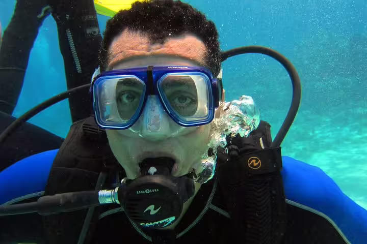New scuba diver breathing from regulator during intro diving and snorkeling day trip in turquoise water