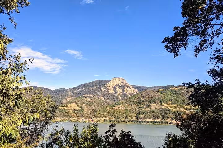 Scenic view of the Iron Gate Gorge with lush greenery and a striking rock formation under a clear blue sky along the Danube.