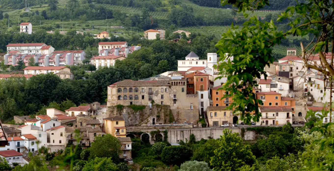 Panoramic view of a hilltop village in Irpinia, Italy, surrounded by lush green vineyards and countryside landscapes