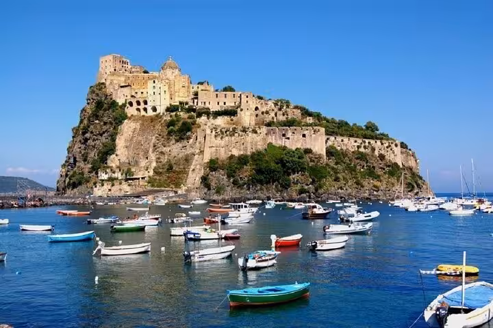 Scenic view of Ischia's Aragonese Castle with colorful boats in the foreground, perfect for a Naples island tour.