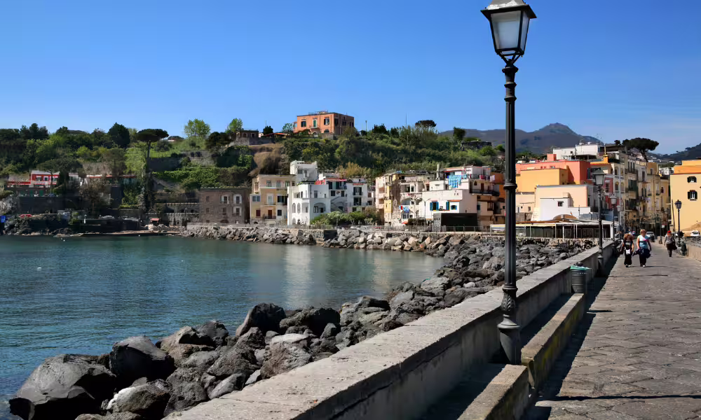 Colorful houses and waterfront promenade in Ischia Porto, Italy, viewed from the sea on a sunny coastal walking tour