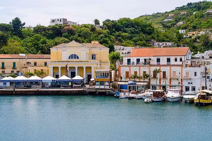Charming waterfront scene in Ischia with colorful buildings, boats, and lush hills, perfect for a relaxing day trip.
