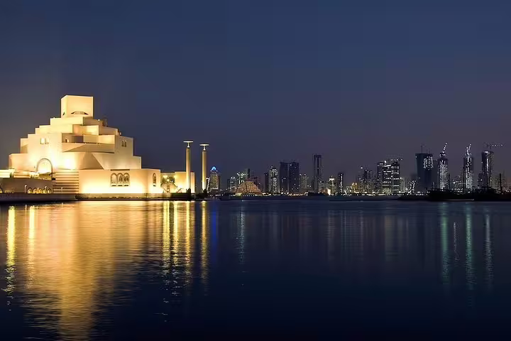 Museum of Islamic Art in Doha glowing at night, reflecting over the water with cityscape backdrop on night tour.