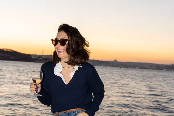 Guest holding a glass of wine on an Istanbul Bosphorus sunset cruise, enjoying golden-hour views