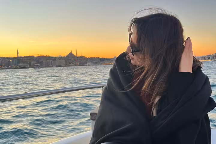 Woman on deck during Istanbul Bosphorus sunset cruise, skyline and mosques in view, luxury yacht wine experience