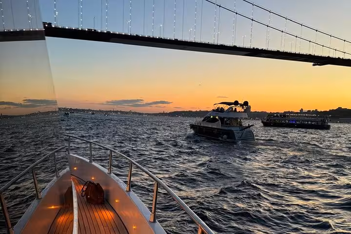 Luxury yacht bow under the Bosphorus Bridge at sunset in Istanbul, scenic Bosphorus cruise with wine