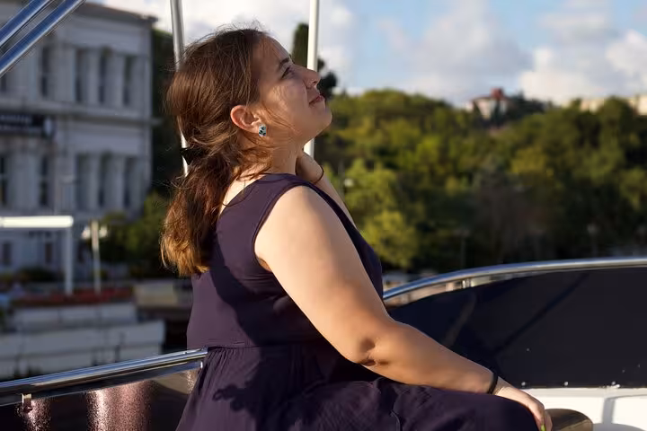 Woman relaxing on yacht deck during Istanbul Bosphorus sunset cruise, scenic waterfront in golden light