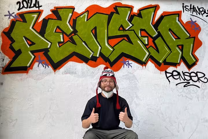 Guest posing with thumbs up by bold graffiti during Istanbul street art experience with local artists