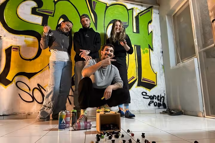 Group of local artists and guests posing with spray cans by colorful mural at Istanbul home garden street art tour