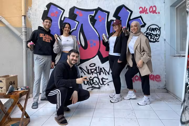 Group holding spray cans in front of finished mural at Istanbul Street Art Experience with local artists at home garden