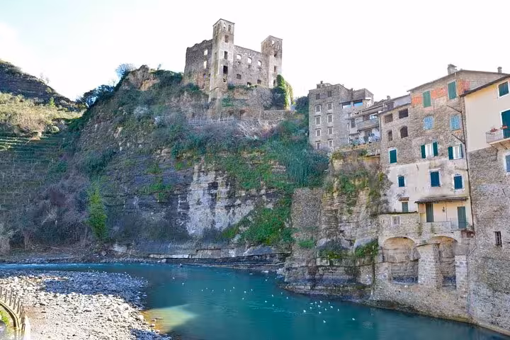 Historic castle ruins perched on a cliff above a serene river in an Italian town, showcasing stunning architecture.