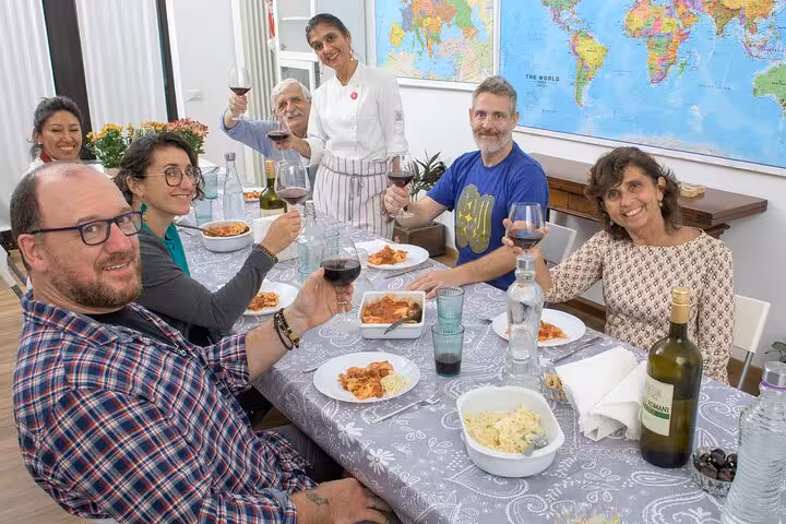 Group of people enjoying a homemade Italian meal with an Italian chef, toasting with wine around a dining table.
