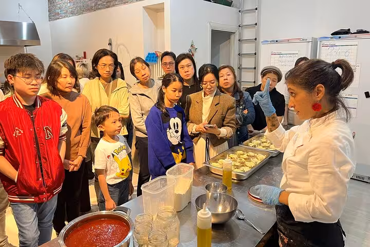 Group attentively follows Italian chef's live cooking demo, learning authentic recipes in a cozy kitchen setting.