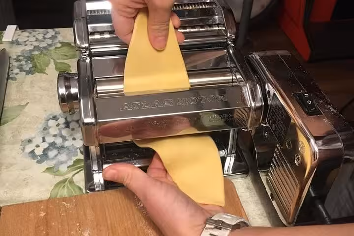 Hands guiding pasta dough through a traditional pasta machine during an Italian culinary workshop.