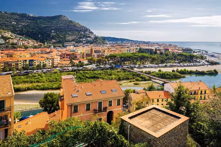 Panoramic view of an Italian coastal city with terracotta rooftops and lush greenery by the sea.