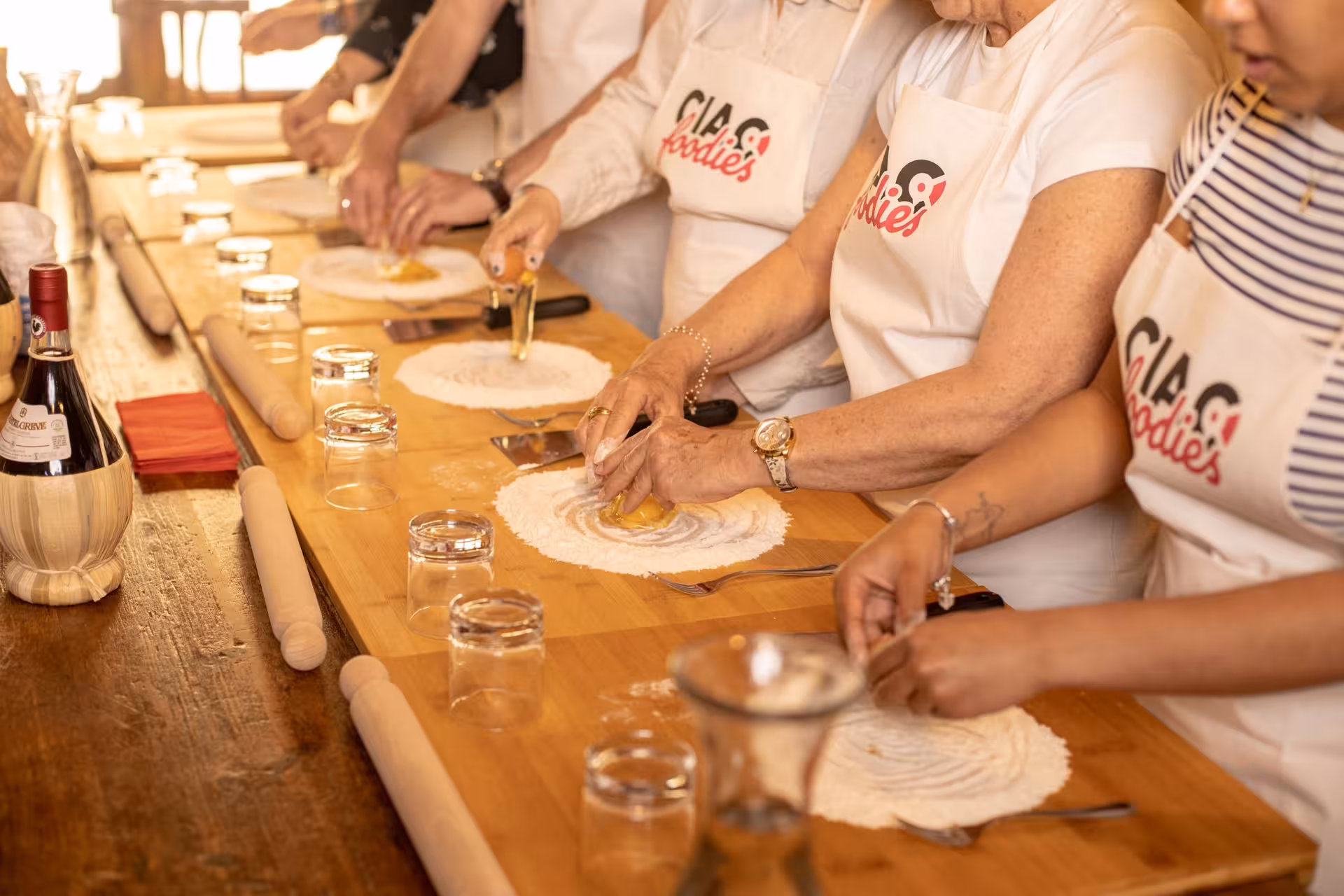 Participants in an Italian cooking class crafting pasta dough, surrounded by wine bottles and rolling pins.