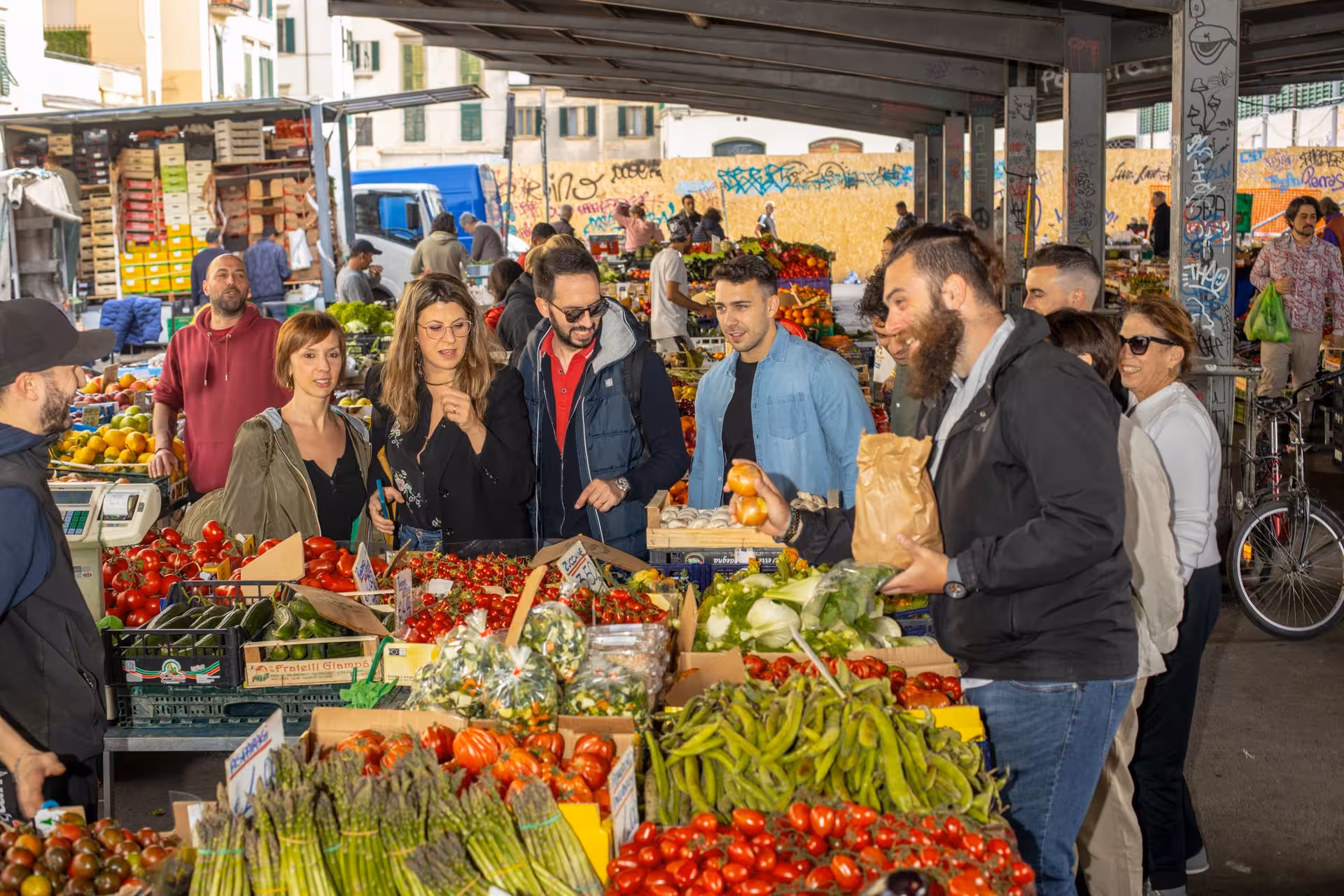 Group of people exploring a vibrant Italian grocery market during a cooking masterclass tour experience.