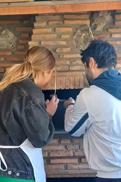 Couple checks the wood-fired oven during Italian farm tour pizza experience with cheese tasting, wine and limoncello