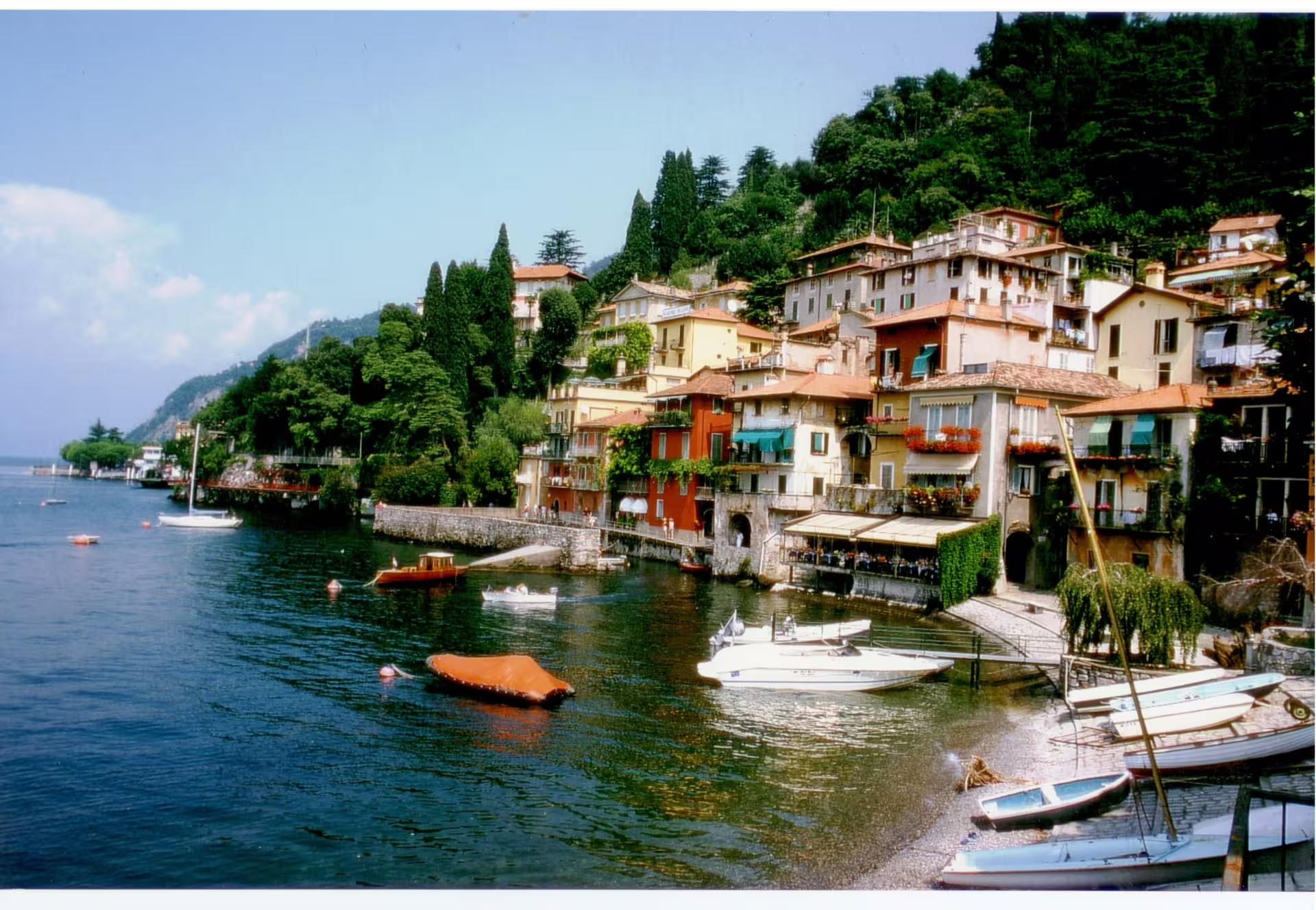 Colorful hillside village with boats moored on a tranquil lake, featured on an Italian Great Lakes culinary self-drive itinerary