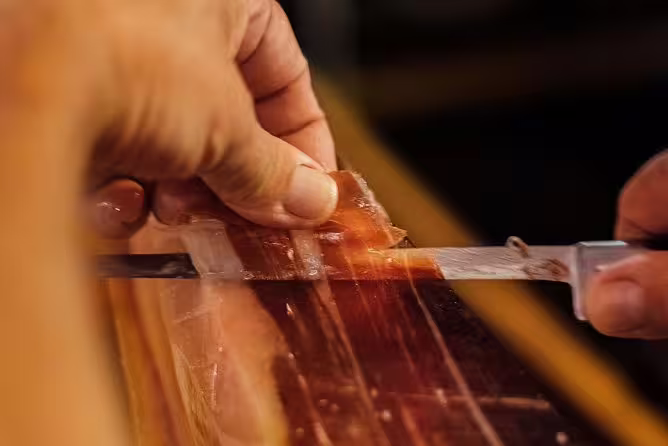 Close-up of hands expertly slicing jamón ibérico, showcasing artisanal Spanish charcuterie skills.
