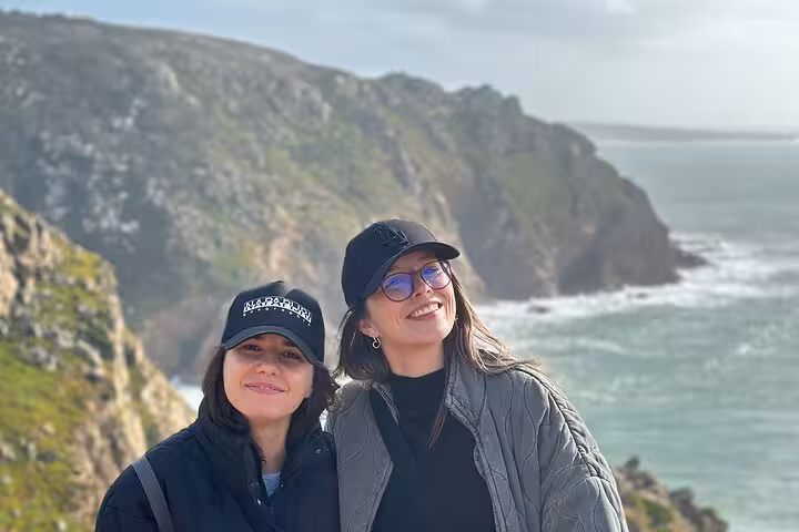 Two smiling tourists at Cabo da Roca, enjoying the stunning Atlantic coastal views on a sunny day.